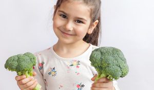 A little smiling girl holding green vegetable in hands