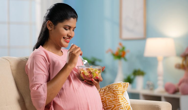 A happy pregnant woman eating protein-rich food from a bowl